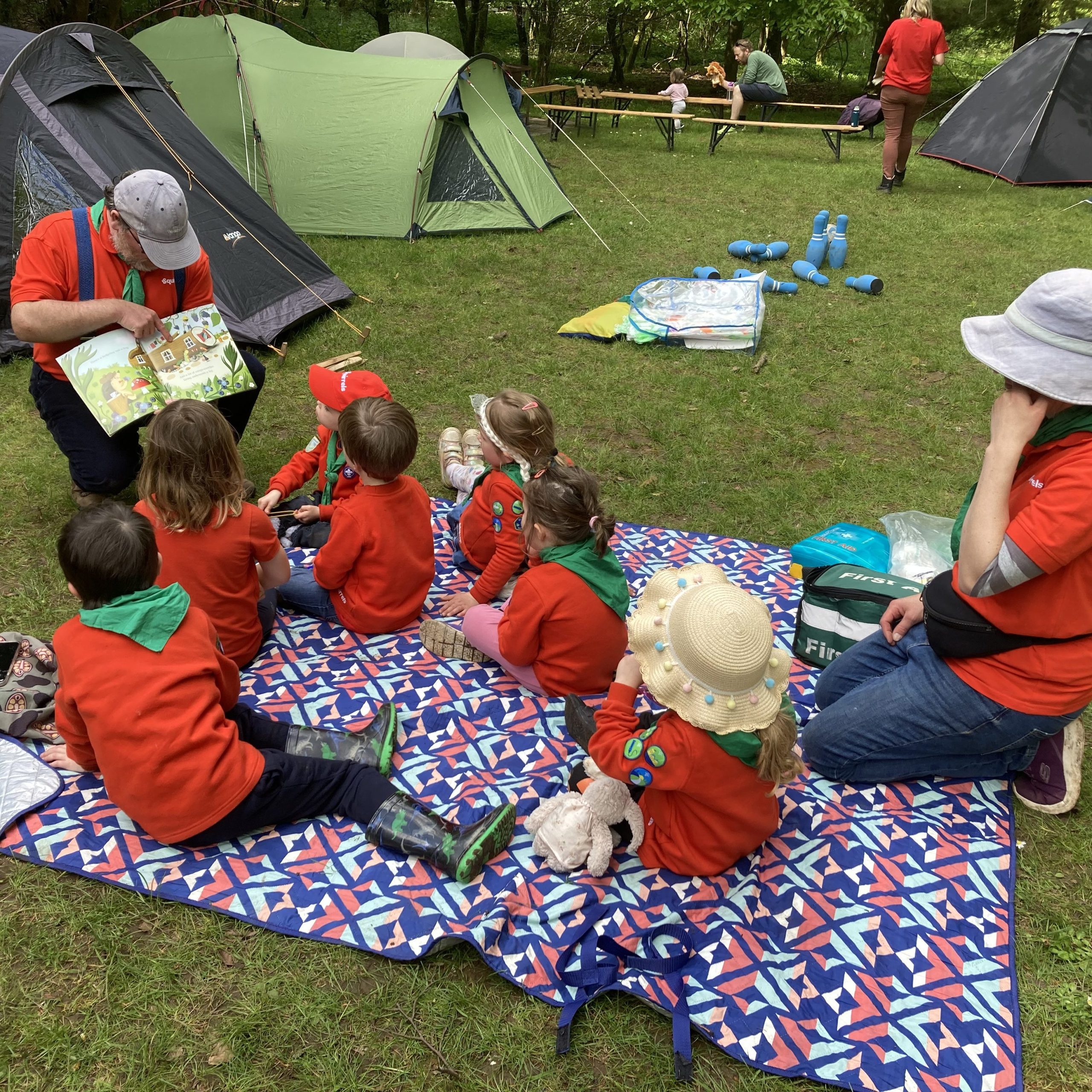 Squirrel scouts sitting on a blanket outside at a camp, listening to a story